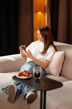 Genç kadın boş vakitlerinde kanepede oturuyor ve telefonunu kaydırıyor..