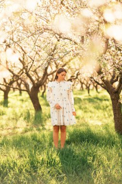 Güzel güneşli bir günde badem bahçesinde duran beyaz elbiseli genç bir kadın..