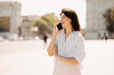 Neşeli genç kadın akıllı telefonunu kontrol ederken şehirde yürüyor..