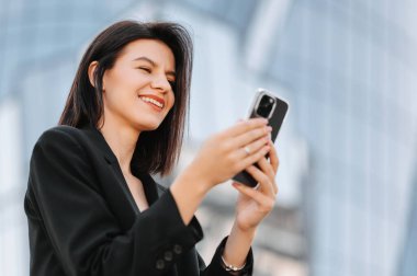 Açık havada akıllı telefonunu kullanan gülümseyen genç bir kadının yakın plan fotoğrafı..