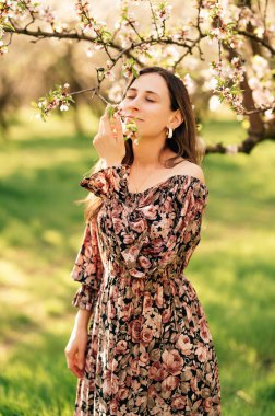 Meyve bahçesindeki badem çiçeklerinin kokusundan hoşlanan genç bir kadının dikey portresi..