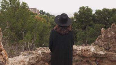 Siyah şapkalı ve paltolu kadın manzarası sakin manzaralı taş balkondan doğa manzarasına hayran.