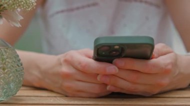 Arkaplanda dekoratif vazo bulunan ahşap bir masada akıllı telefon kullanan insanların yakın plan görüntüsü..