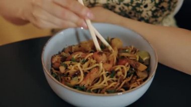 Yemek çubuklarıyla bir kase Asya usulü kızarmış erişte yiyen birinin yakın çekimi. Yemek ve mutfak içeriği için ideal.