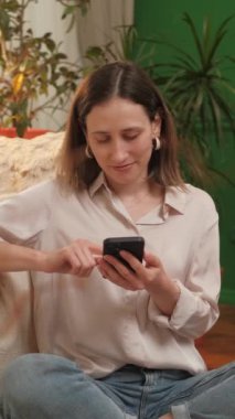 Evindeki bir kanepede oturan genç bir kadın, bitkilerle çevriliyken akıllı telefonunu rahatça kullanıyor..