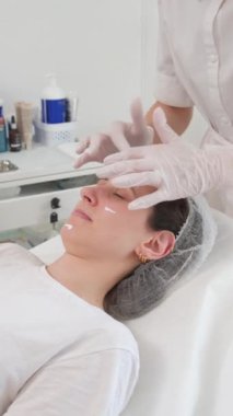 Bir kadın, modern bir klinikte koruyucu eldiven giyen bir uzman tarafından profesyonel bir yüz tedavisi görüyor.
