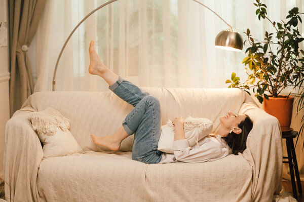 A woman is luxuriously lounging on a sofa with a pillow in a warm living space, radiating comfort and relaxation