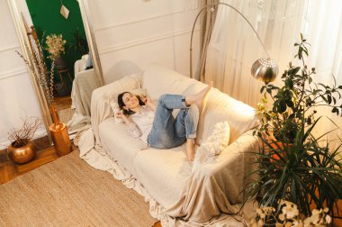 Rahat bir kanepede, yeşil ve sade dekorlu bir oturma odasında dinlenen bir kadın..