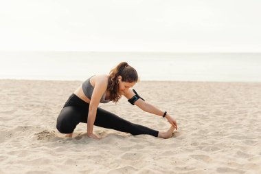 Bir kadın açık hava antrenmanı sırasında kumlu bir plajda spor yapıyor..