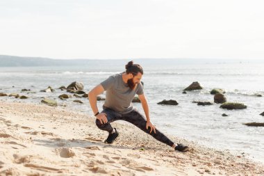 Arka planda kayalık bir kıyı şeridi olan kumsalda uzanan adam spor ve rahatlamaya odaklanıyor..