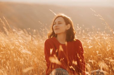 Gün batımında altın bir tarlada huzur ve sükunet saçan bir kadın, doğası gereği güzelliklerle çevrili.