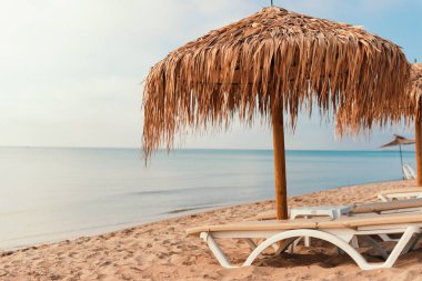 Saman şemsiyeli, güneşli ve sakin deniz manzaralı sakin sahil manzarası rahatlatıcı bir tatil için mükemmel bir kaçış sunuyor.