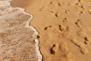 Okyanus dalgaları yaklaşırken kumlu sahilde bırakılan ayak izleri günbatımında huzurlu bir sahili yakalıyor..