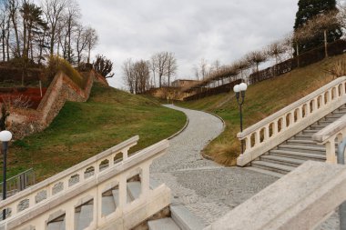 Dolambaçlı bir patika, bulutlu bir gökyüzünün altındaki taş merdivenlerle manzaralı bir açık hava yaratıyor.