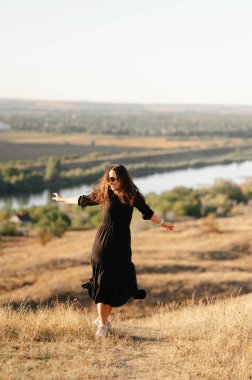 Bir kadın kollarını bir tepenin üzerine uzatmış güneşin batışında doğanın güzelliğinin tadını çıkarıyor.