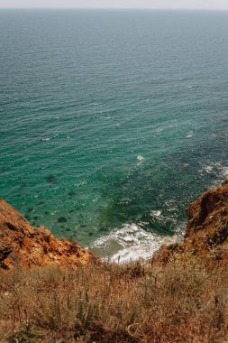 Berrak, turkuaz okyanus sularına bakan bir uçurumdan sakin bir manzara ve aşağıdaki engebeli kayalık kıyı şeridi..
