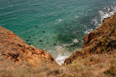 Güzel bir günde, berrak bir gökyüzünün altında dalgalı denizle buluşan engebeli kıyı uçurumlarının çarpıcı manzarası.