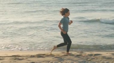 Bir kadın gün batımında plajda koşuyor, sağlıklı bir yaşam tarzını kucaklıyor ve açık hava egzersizinin tadını çıkarıyor.