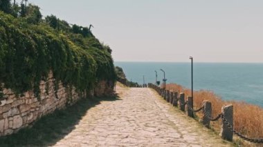 Kıyı boyunca uzanan güzel taş patika, yemyeşil, berrak bir gökyüzünün altında okyanusa bakıyor..