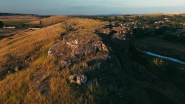 Değişik manzaralara sahip, altın bir günbatımı gökyüzü altında kayalık arazisi olan yuvarlanan tepelerin panoramik bir görüntüsü..