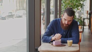 Modern bir kafede, sakallı bir adam güzel kokulu kahveyle lezzetli bir dilim pastanın tadını çıkarmaktan zevk alır.