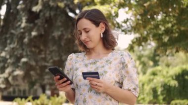 Çevrimiçi alışveriş yapan genç bir kadın akıllı telefonu ve ödeme kartıyla dışarıda eğleniyor.