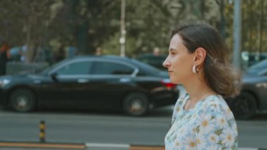 Çiçekli elbiseli bir kadın renkli bir şehir sokağında geziyor, şehir hayatının canlı özünü somutlaştırıyor.