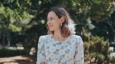 Modayı takip eden, şık çiçekli kıyafetli neşeli bir kadın canlı yeşillikler arasında zarif bir şekilde duruyor, mutluluk saçıyor.