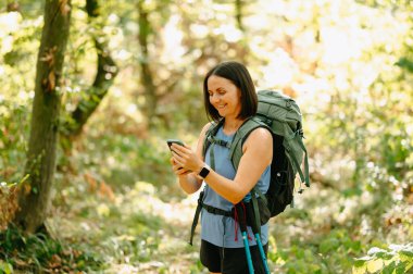 Bir yürüyüşçü akıllı telefonunu kontrol ederken çarpıcı bir orman ortamında doğanın güzelliğinin tadını çıkarıyor.