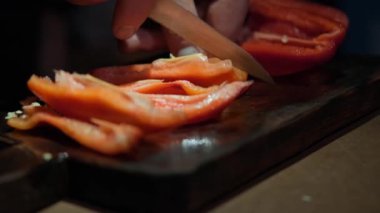 Tahta bir yüzey üzerinde canlı kırmızı dolma biberleri ustalıkla dilimleyen bir eli gösteren detaylı bir yakın çekim.