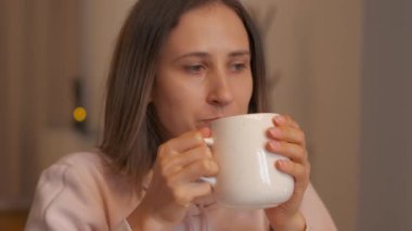 Bir kadın, huzurlu bir ortamda, düşüncelerini yansıtan beyaz bir kupadan yudumluyor.