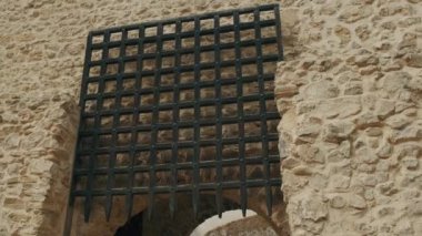 Karmaşık bir şekilde tasarlanmış demir kapı, zarif ortaçağ mimarisi sergilenen, dokulu taş bir duvarda sergileniyor.