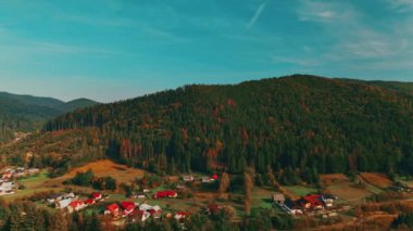 Parlak mavi gökyüzünün altındaki yemyeşil tepelerin ve ağaçların arasında yuva yapmış tuhaf bir köyün resimsel manzarası.