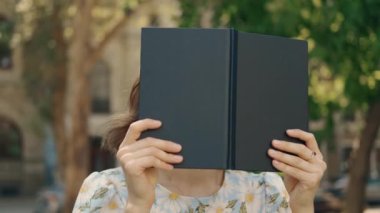 Güneşli bir parkta oturan bir kadın gururla elinde kara bir kitapla anın tadını çıkartıyor.