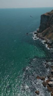 Parlak turkuaz suların sergilendiği nefes kesici bir sahil manzarası ve yanında uzaktaki görkemli uçurumlar.