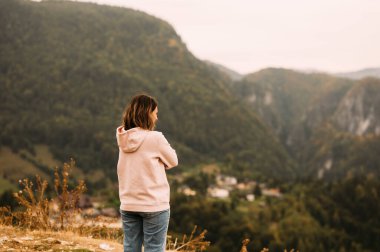 Bir kadın, görkemli dağlar ve bereketli doğa ile çevrili güzel, sakin bir manzarayı yansıtmak için bir dakikasını ayırır.