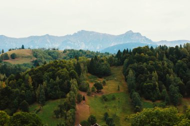 Görkemli, bulutlu bir gökyüzünün altındaki yüksek dağlarla çevrili yemyeşil tepelerin nefes kesen huzurlu manzarası.
