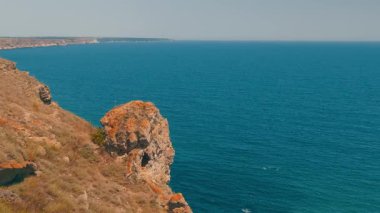 Nefes kesici bir kıyı manzarası engebeli kayalıkları sergiliyor berrak bir gökyüzünün altında sakin mavi sularla eşleştiriyor.