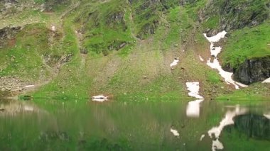 Güzel, dingin bir dağ gölü yemyeşil ve kalan karları derinden yansıtır. Muazzam bir huzuru çağrıştırır.