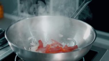 Gümüş bir tavada taze sebzeler hazırlayan bir şef. Buhar yükseliyor, canlı bir yemek sahnesi sergiliyor..