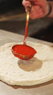Yetenekli bir şef taze pizza hamuruna canlı domates sosu sürüp lezzetli ve doyurucu bir yemek hazırlar.