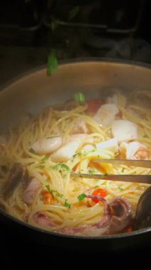 Renkli ve canlı bir spagetti görüntüsü. Deniz ürünleri bir tencerede ustalıkla pişiriliyor. Güzel mutfak sanatları sergiliyor.