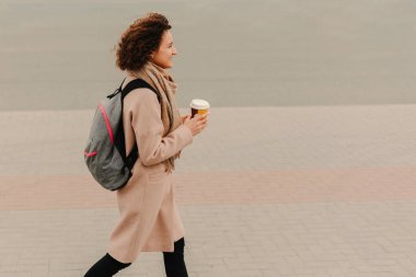 Şık bir kadın hareketli caddelerde rahatça yürüyor, kahveden zevk alıyor ve canlı şehir modasını sergiliyor.