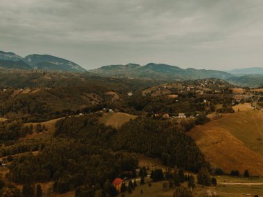 Bulutlu gökyüzünün altındaki yemyeşil tepelerin ve dağların sakin manzarası, doğa temalı projeler için mükemmel..