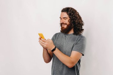 Kıvırcık saçlı neşeli bir adam şu anda mutlu bir şekilde akıllı telefon cihazıyla meşgul.