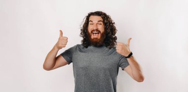 Kıvırcık saçlı neşeli ve neşeli bir adam, parlak stüdyo ortamında mutlu bir jest yapıyor.