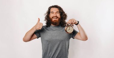 Neşeli bir adam, etkili zaman yönetimini sembolize eden bir çalar saati tutarken başparmağını kaldırır.