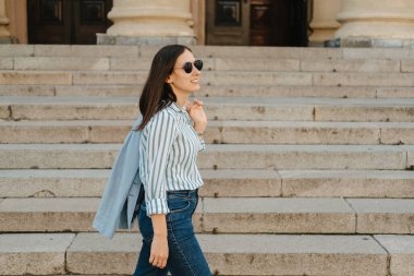 Şık bir kadın hareketli bir şehirde taş basamaklardan aşağı iniyor, zarif ve modaya uygun tarzını sergiliyor