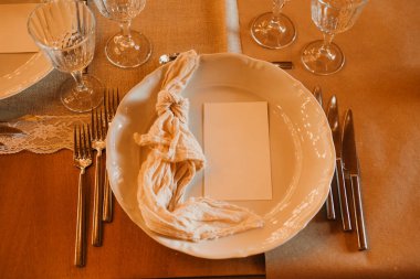 Zarif bir şekilde düzenlenmiş masa seti dekoratif bir peçete sergiliyor yanında zarif ve ince bir cam eşliğinde.