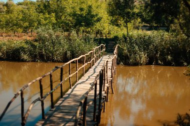 Canlı yeşilliklerle çevrili sakin bir su yolunu zarif bir şekilde geçen güzel, ahşap bir köprü.